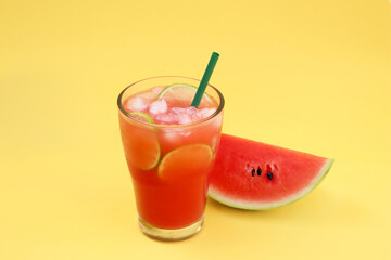 Glass of delicious drink with lime slices, ice cubes and fresh watermelon on yellow background