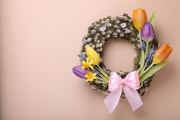 Willow wreath with different beautiful flowers and pink bow on beige background, top view. Space for text © New Africa