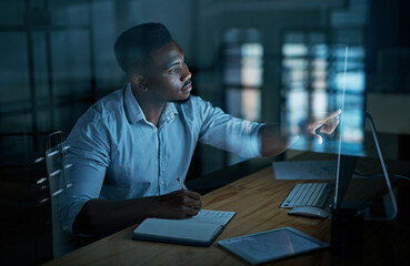 Having goals gives you focus. a young businessman writing in a notebook and using a computer during a late night at work.