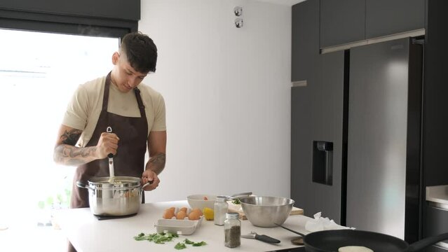 Young Ecuadorian man mashing potatoes to prepare llapingachos at kitchen.