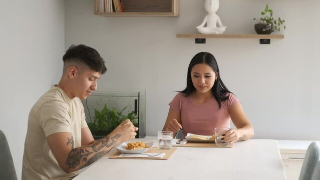 Two young hispanic people eating traditional arepas in the living room.