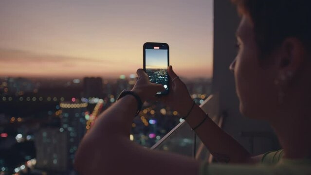 happy woman using smartphone taking photo of beautiful sunset enjoying sharing summer vacation travel experience on balcony
