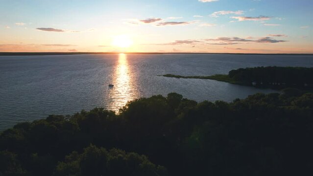 People who are relaxing on the beach by the body of water are enjoying the magnificent sight of the sunset, which creates an unparalleled atmosphere and contributes to relaxation.
