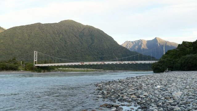 Time lapse of colourful sunset over mountains around long, old steel bridge