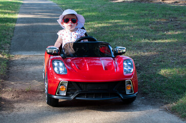 Fototapeta premium Caucasian baby in a white hat riding in an electric convertible red sport car. child driving a car on a summer day
