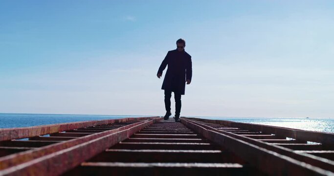 Man reaches edge horizon bridge turns around slowly wearily walks back along bridge rails sea sky sunset. Achieving a dream is a difficult path disappointment. Aesthetics waiting gait Generative AI