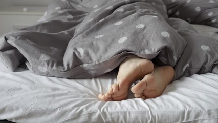 Woman's feet poking out from beneath a warm blanket, as she adjusts her body and prepares for a peaceful day of rest