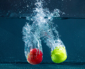 Red and green Apples splashing into water on a black background, fishing tank exposed shooting in...