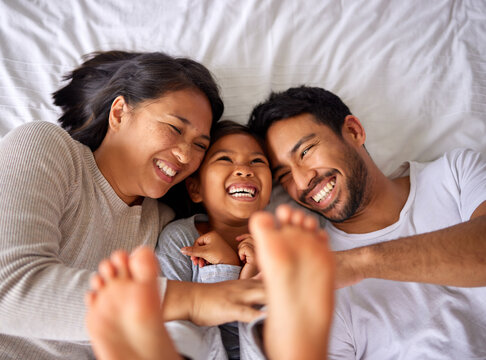 Family Of Three Laughing And Having Fun While Lying In A Bed Together