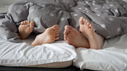 Closeup of couple's feet lying on bed and gently touching each other. Concept of love, relations and having good time together