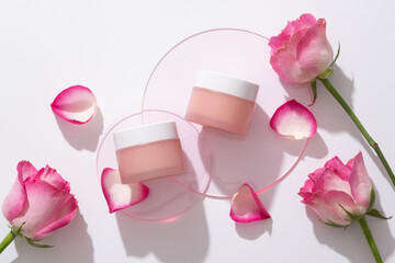 Mockup scene for cosmetic of rose extract with two pink cream jars on round acrylic sheets on white background with fresh rose and rose petals. Space for design, branding product