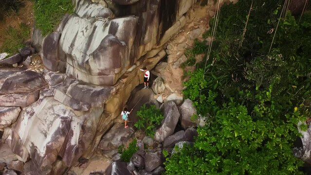 Man and woman are doing mountaineering holding the cord filmed by drone. Caucasian couple are climbing rock consisting of huge stones. Endurance and courage during travelling and walking on cliffs