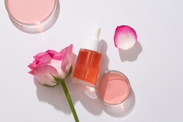 Flat lay cosmetic mockup with glass bottle and dropper cap containing pink liquid, fresh rose and...