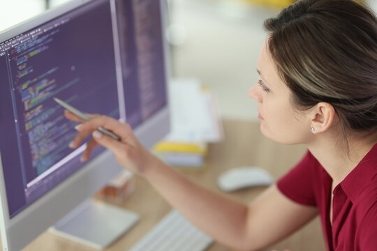 Woman checks code pointing pen to screen of computer