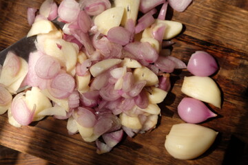 Sliced onion and garlic on a wooden cutting board. stainless steel knife for slicing. served on a rustic brown wooden table. Onion and garlic are spices for cooking. bawang merah, bawang putih iris.
