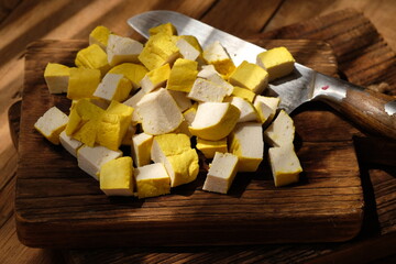 sliced yellow tofu on a teak wood cutting board. stainless steel blade. soy bean products.