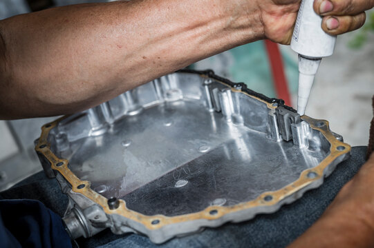Auto mechanic applying black high-temp RTV silicone gasket maker to oil pan flange.	