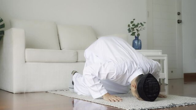 Asian Muslim man reciting surah al-Fatiha passage of the Qur'an, in a daily prayer at home in a single act of sujud called a sajdah or prostration. Quran holy book is a public item of all Muslim