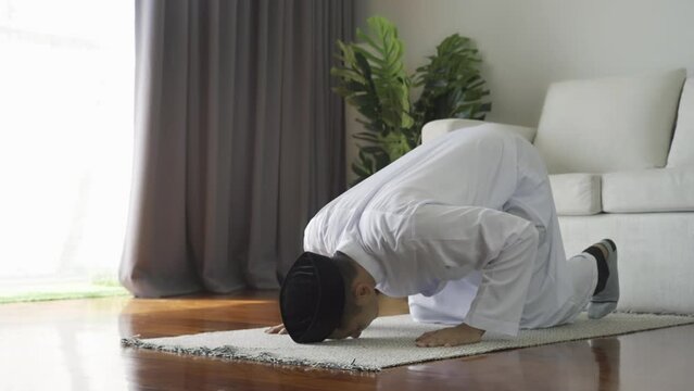 Asian Muslim man reciting surah al-Fatiha passage of the Qur'an, in a daily prayer at home in a single act of sujud called a sajdah or prostration. Quran holy book is a public item of all Muslim