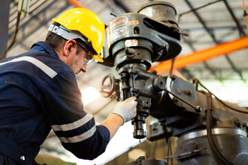 Professional caucasian white ethnicity male technician operating the heavy duty machine in the lathing factory. Technician in safety and helmet suit controlling a machine in factory.