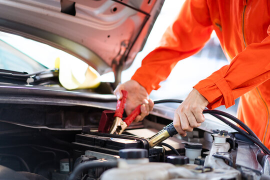 Professional roadside technician support using an emergency jump start cable to connect a battery from other car to the one which out of battery. 