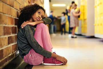 School really isnt for me. Full length shot of a young girl sitting in the hallway at school and feeling depressed. - obrazy, fototapety, plakaty