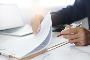 Asian businessman reviewing document reports at office workplace with computer laptop. legal expert, professional lawyer reading and checking financial documents with chart or insurance contract