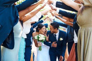 Wedding guests forming a tunnel with their hands as newlywed couple walk through it. Bride and...