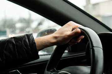 Selective focus man's hand on steering wheel, driving car in winter background. Black luxury modern...
