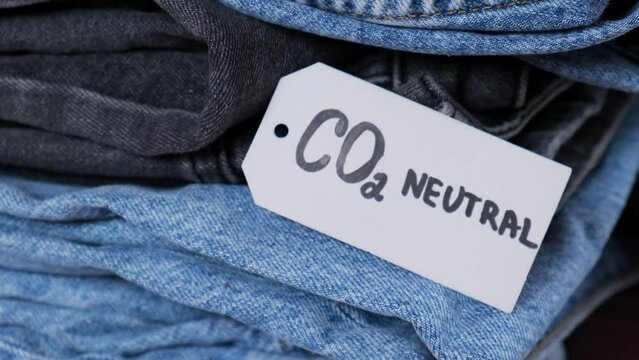 CO2 neutral emission text note on stack of jeans. Ecology nature friendly, climate change, green fuel and earth protect concept. Carbon emission paper recycled label. Natural organic jeans clothing