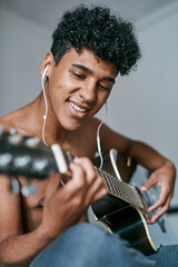 The best time to build your skills is now. a young man using earbuds while playing the guitar at home.