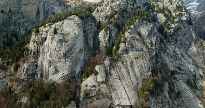Aerial pullback view of a rugged mountain and boulders covered in pine trees in Val di Mello, Italy.