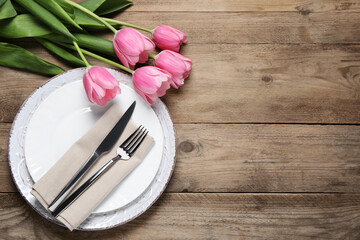 Stylish table setting with cutlery and tulips on wooden background, flat lay. Space for text
