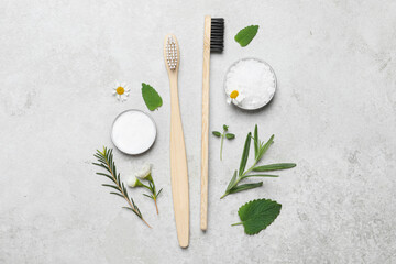 Fototapeta na wymiar Bamboo toothbrushes, flowers and herbs on light grey table, flat lay