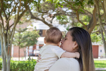 Fototapeta premium Madre cargando a su bebé en un parque, día soleado, tonos cálidos