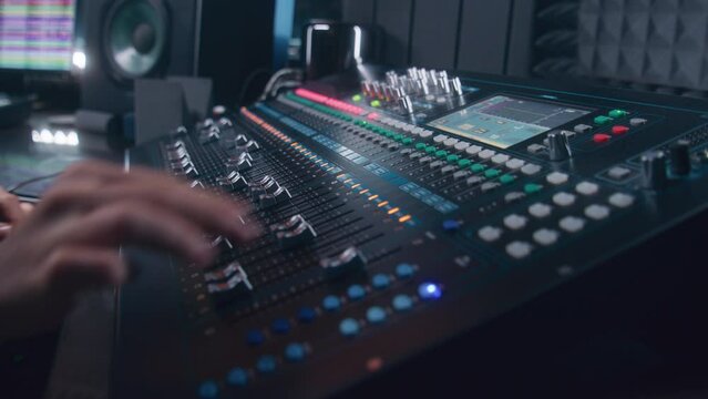 Audio engineer uses mixing console, remote control for adjusting sound, audio mixer. Musician changes the volume level, creates song with modern equipment. Sound recording studio. Music production.