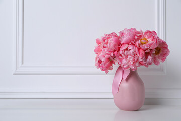 Beautiful bouquet of pink peonies in vase near white wall. Space for text