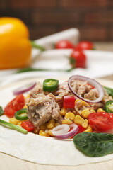 Delicious tortilla with tuna and vegetables on wooden board, closeup. Cooking shawarma