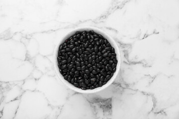 Bowl of raw black beans on white marble table, top view