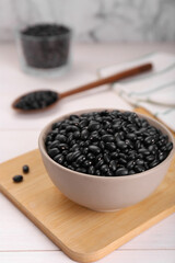 Bowl of raw black beans on white wooden table, closeup