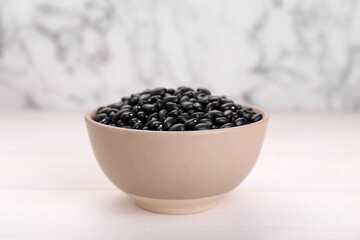 Fototapeta na wymiar Bowl of raw black beans on white wooden table