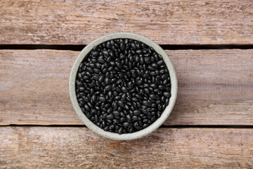 Bowl of raw black beans on wooden table, top view
