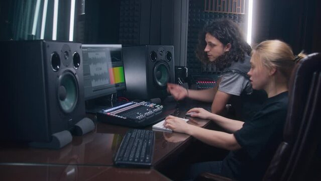 Female audio engineer and singer create song in music recording room. Computer screen showing program interface and tools for creating music. Modern sound recording studio equipment. Music production.