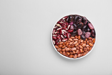 Different kinds of kidney beans in bowl on white background, top view. Space for text