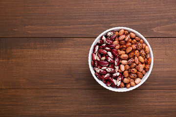 Different kinds of dry kidney beans in bowl on wooden table, top view. Space for text
