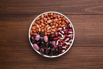 Different kinds of dry kidney beans in bowl on wooden table, top view