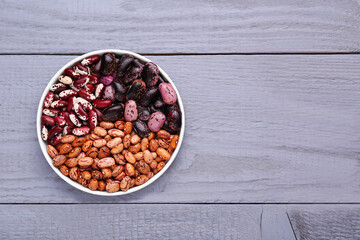 Different kinds of dry kidney beans in bowl on light grey wooden table, top view. Space for text