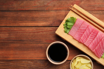 Tasty sashimi (pieces of fresh raw tuna), lettuce, soy sauce and ginger slices on wooden table,...