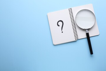 Magnifying glass and notebook with question mark on light blue background, top view. Space for text