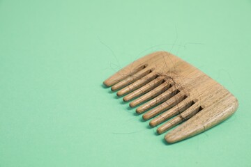 Wooden comb with lost hair on green background. Space for text